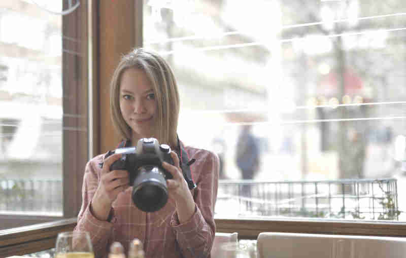 Cheerful young woman with advanced camera in cafe