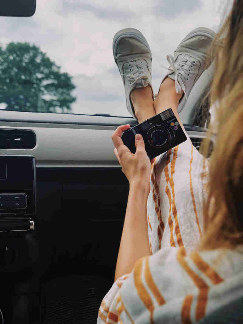 women holding compact camera while feet on car dashboard 